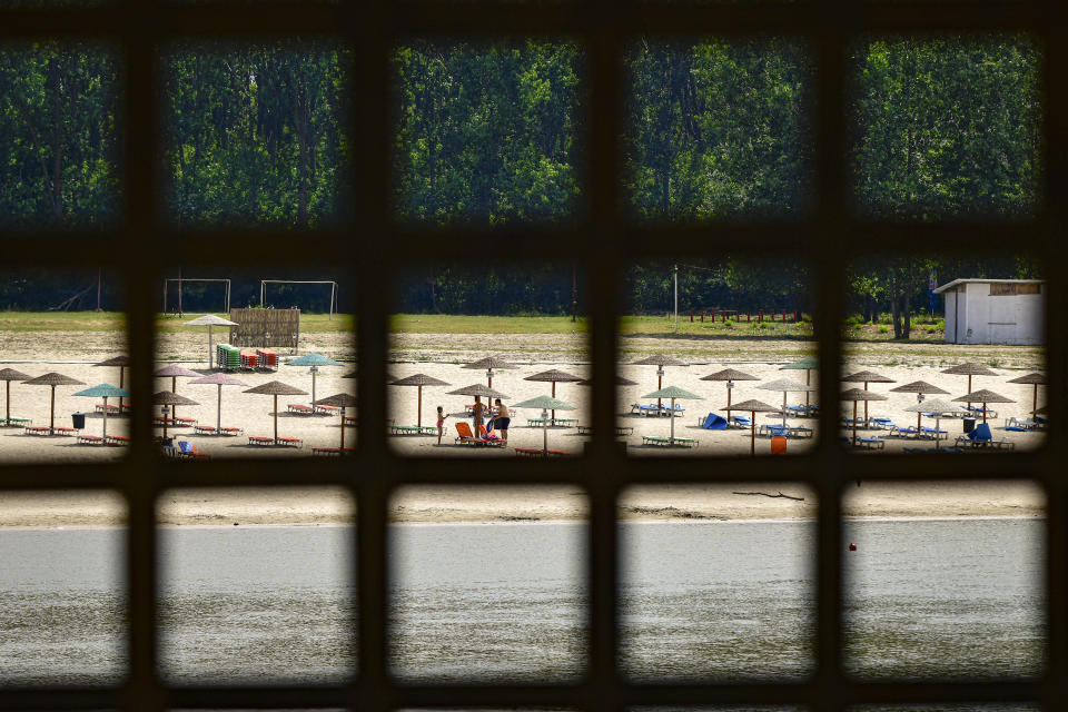 A family stands under an umbrella on a beach on the river Danube banks in Calarasi, southern Romania, the hometown of Claudia Anghel, a Romanian midwife working in England, on Monday, July, 27, 2020. Romania joined the European Union in 2007 and, by 2013, more than 14,000 Romanian doctors were working abroad, about 26% of the country's total number of physicians. (AP Photo/Andreea Alexandru)