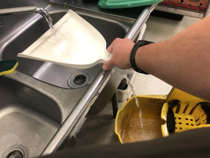 Someone using a dust pan to fill a mop bucket