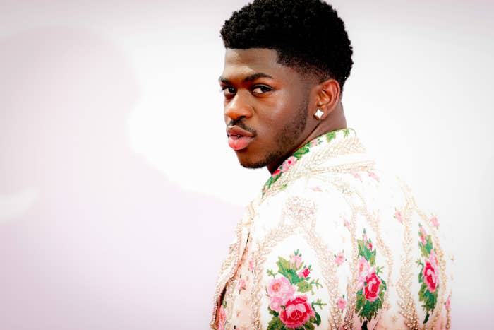 Lil' Nas looking over his shoulder in an embroidered floral print jacket