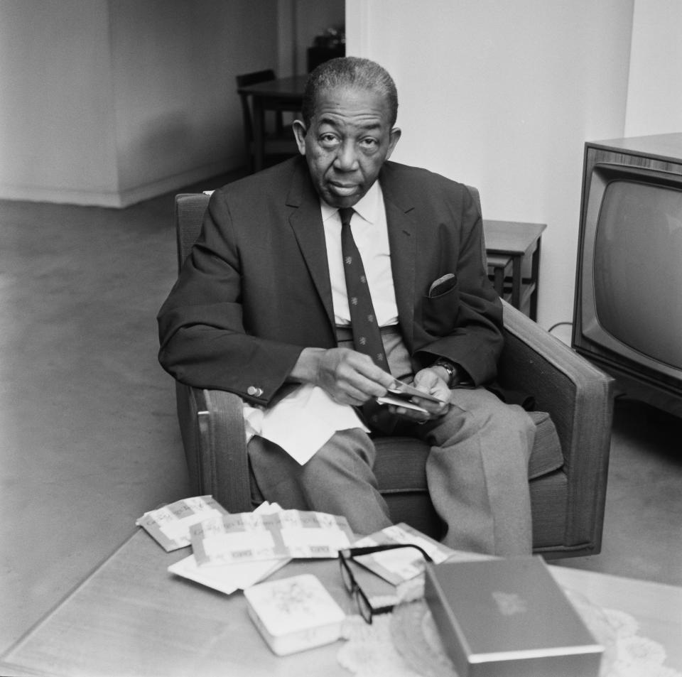 West Indian cricketer and politician Learie Constantine sits in an armchair with documents in front of him