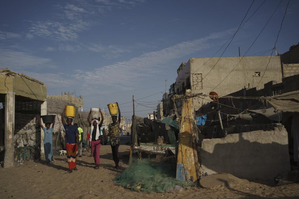 Young women carry buckets of waste before throwing them away next to the ocean waters at a beach in Saint Louis, Senegal, Tuesday, Jan. 17, 2023. Officials promised the drilling in the area would soon bring thousands of jobs and diversification of the economy. Instead, residents say, the rig has brought only a wave of problems, unemployment and more poverty. (AP Photo/Leo Correa)