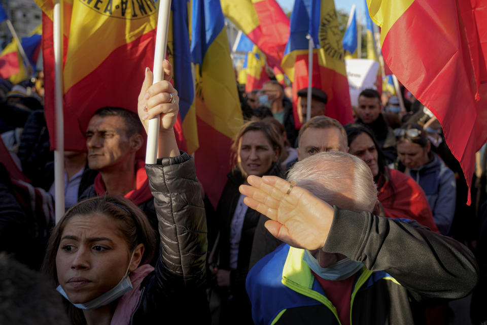 A man shields his face from the sun as people wave flags during an anti-government protest organised by the far-right Alliance for the Unity of Romanians or AUR, in Bucharest, Romania, Saturday, Oct. 2, 2021. Thousands took to the streets calling for the government's resignation, as Romania reported 12,590 new COVID-19 infections in the past 24 hour interval, the highest ever daily number since the start of the pandemic. (AP Photo/Vadim Ghirda)