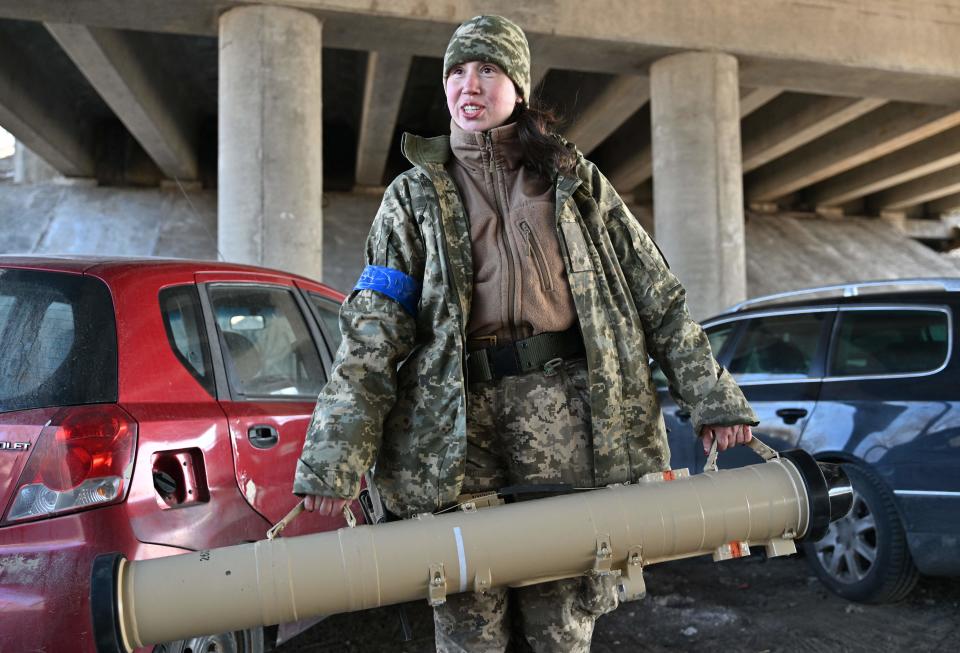 With one strap in each hand, Tetiana Chornovol, in camouflage jacket and hat, holds carries an anti-tank guided missile.