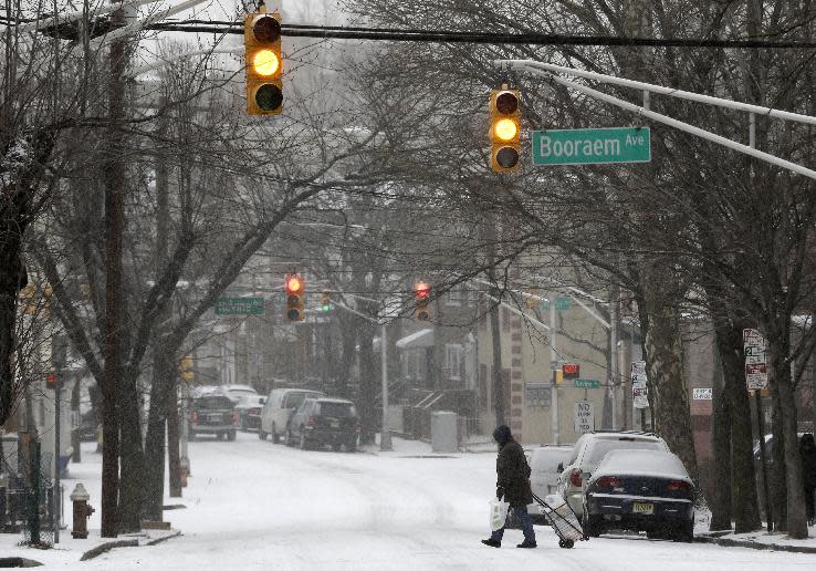 A woman pulls a cart as she walks across the street covered with snow, Tuesday, Jan. 21, 2014, in Jersey City, N.J. A storm is expected to hit the northern New Jersey region throughout the day. Because of hazardous driving conditions New Jersey Gov. Chris Christie's inauguration party at Ellis Island was cancelled. (AP Photo/Julio Cortez)