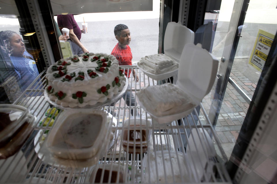 In this Monday, July 1, 2019 photo passers-by walk near an entrance of a Latin-style cafe that features a display of cakes and pastries in a window, in Chelsea, Mass. A recent study by the Pew Research Center shows the number of Central Americans in the United States increased over the last decade. Chelsea has exemplified that trend with a population that is more than 60 percent Latino. (AP Photo/Steven Senne)