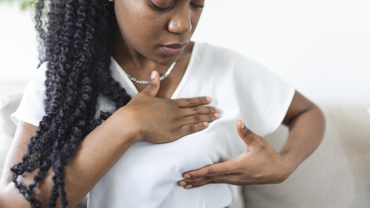 A Black woman palpates her breast to check for signs of breast cancer.