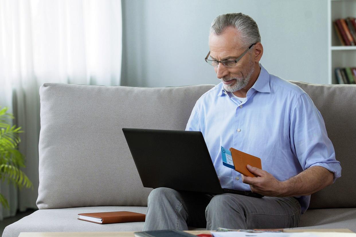 senior looking at computer with passport in hand