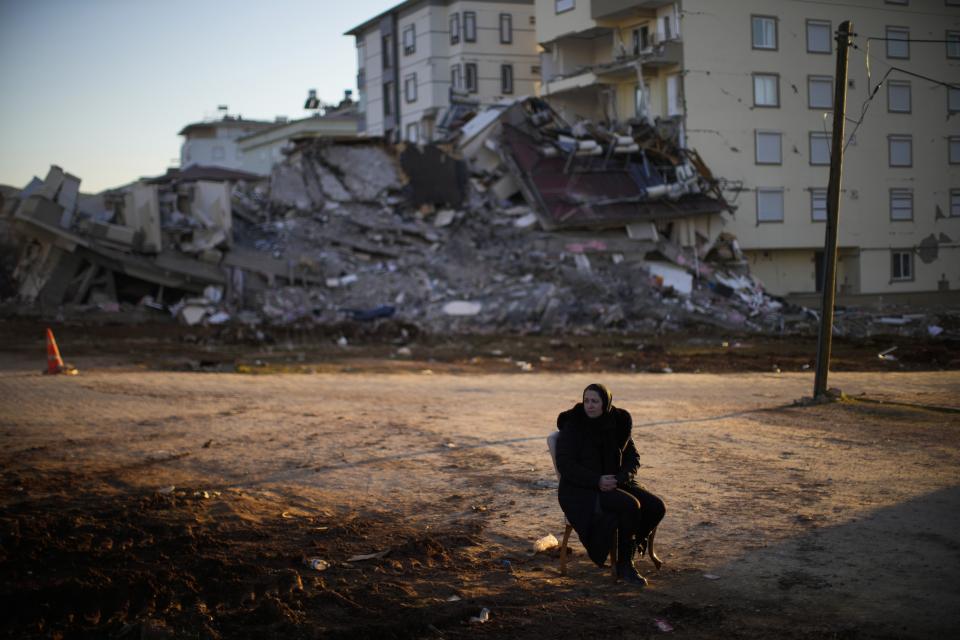 Fatos Baruc, who lives in Germany and whose mother-in-law survived the earthquake, sits on a chair as she waits for her belongings to take away from a damaged building in Pazarcik, Turkey, Monday, Feb. 13, 2023. Thousands left homeless by a massive earthquake that struck Turkey and Syria a week ago packed into crowded tents or lined up in the streets for hot meals Monday, while the desperate search for anyone still alive likely entered its last hours. (AP Photo/Francisco Seco)