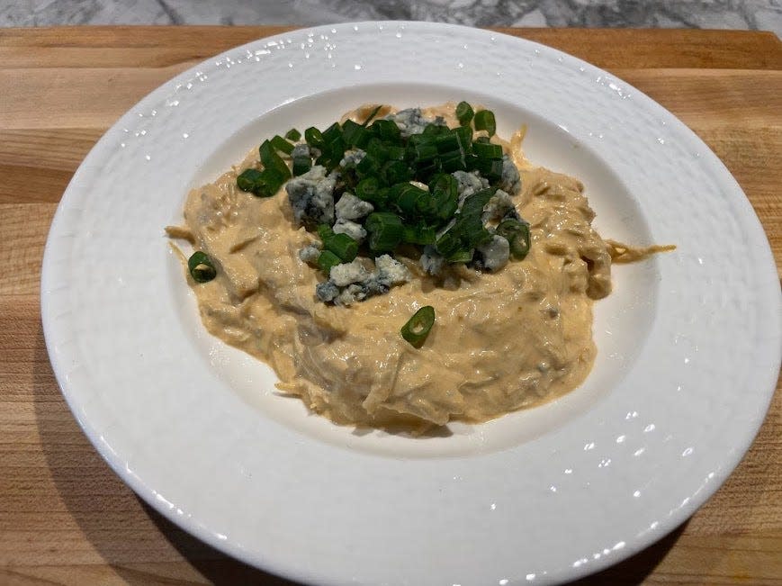 Light-orange Buffalo-chicken dip with visible shreds of chicken on a white plate with scallions and cheese sprinkled on top