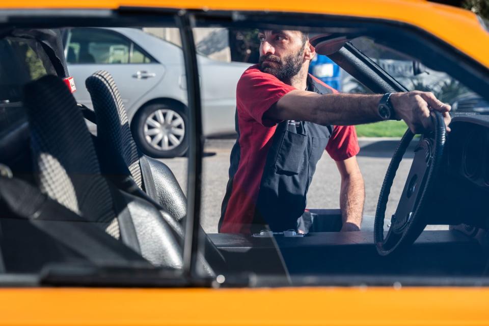 A man reaches into a car to grasp the steering wheel while looking behind him