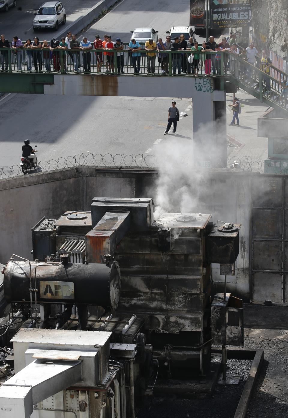 Pedestrians look down at smoldering transformers and electrical equipment at electrical substation in the Baruta area of Caracas, Venezuela, Monday, March 11, 2019. An explosion rocked the power station early Monday, witnesses said, adding to the crisis created by days of nationwide power cuts. (AP Photo/Ariana Cubillos)