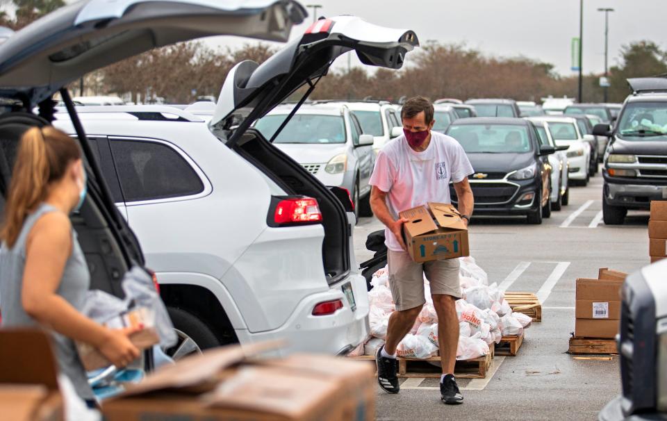 Volunteers load food into cars during the weekly drive-up distribution in West Palm Beach at the Palm Beach Outlets Monday, February 8, 2021. Behind them are cars backed up waiting to join the line. The Tree of Life Resource Center, which offers groceries and other resources to those in need during the COVID-19 pandemic, partners with the mall for the weekly event on Mondays from 8 a.m. to 10 a.m. 