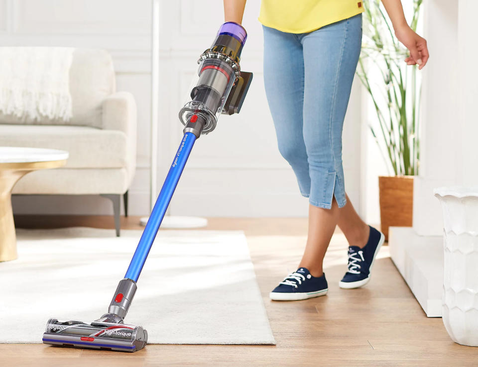 Someone stands while using the Dyson V11 Torque stick vacuum cleaner in their brightly lit living room.