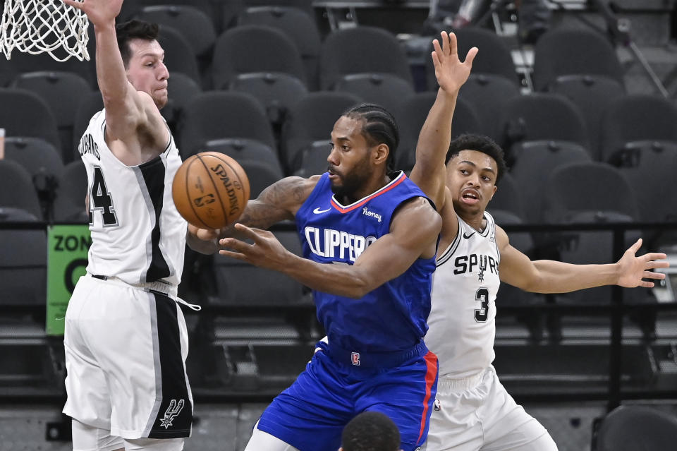 Los Angeles Clippers' Kawhi Leonard, center, passes the ball as he is defended by San Antonio Spurs' Drew Eubanks, left, and Keldon Johnson during the first half of an NBA basketball game on Wednesday, March 24, 2021, in San Antonio. (AP Photo/Darren Abate)