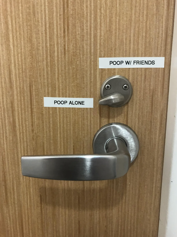 Door with two restroom signs: "Poop Alone" and "Poop W/ Friends." The "Poop W/ Friends" sign is placed above the latch