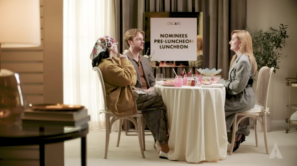 The three seated at a table with drinks and decor, including a sign that reads "Oscars Nominees Pre-Luncheon"