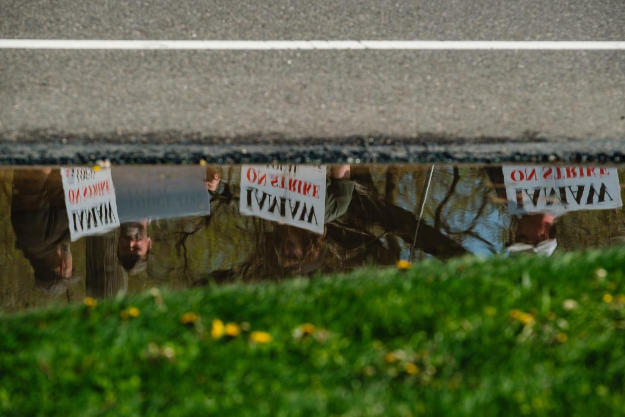 Striking members of the International Association of Machinists and Aerospace Workers Local 1285, employed by Gradall Industries, Inc., are reflected in a puddle while picketing across the street from Gradall, April 15, in New Philadelphia.