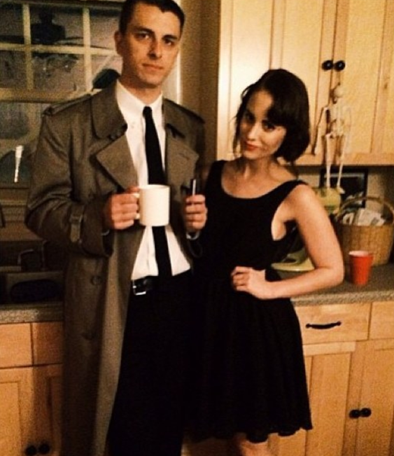 Man in a suit holding a mug standing next to a woman in a sleeveless dress in a kitchen