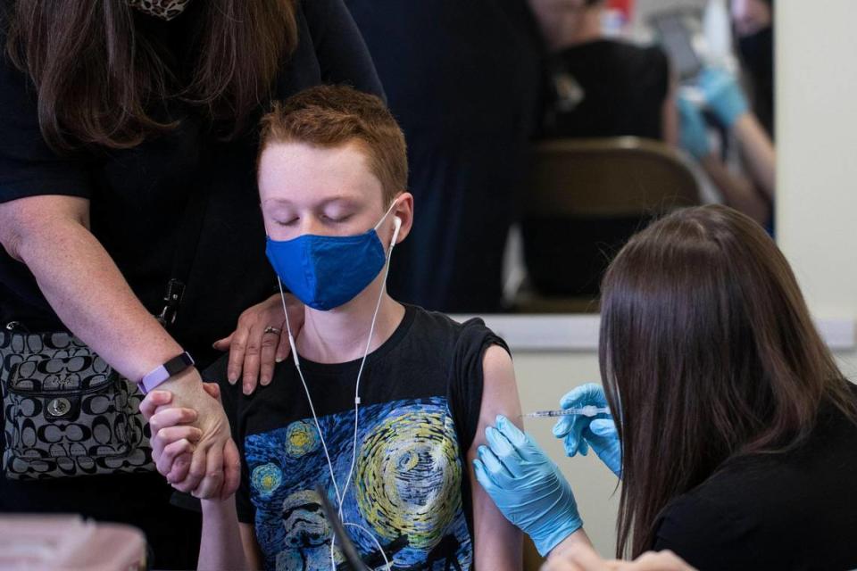 Sean Higgins, 13, closes his eyes, holds hand with his mother and plays music as he receives his first COVID-19 vaccination shot at STEAM Academy in Lexington, Ky., Thursday, May 13, 2021. Higgins was very excited for the possibilities after the shot, but has a fear of needles. ÒIÕll be able to see my friends and family more often,Ó Higgins said.