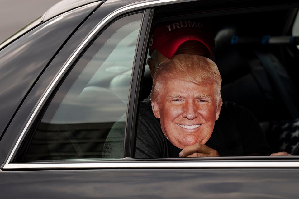 A person holds up a Donald Trump mask.