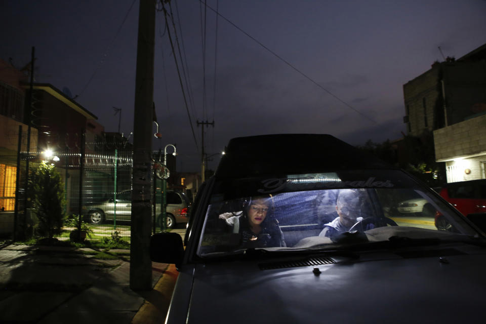 In this Aug. 28, 2019 photo, trans rights activist Kenya Cuevas sits inside her friend's funeral car as she checks her phone messages outside her home in Chalco, Mexico. Because death threats have followed Cuevas since she began to push for protections for trans women, she has enclosed her home with a razor wire fence and set up security cameras. (AP Photo/Ginnette Riquelme)