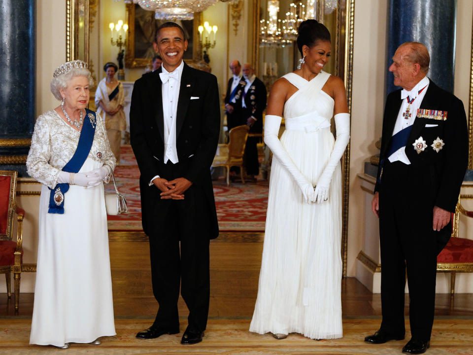 Queen Elizabeth II and President Barack Obama pose with first lady Michelle Obama and Prince Philip, Duke of Edinburgh, in the Music Room of Buckingham Palace ahead of a state banquet on May 24, 2011, in London.   The first lady wore a white gown by American designer Tom Ford, which she paired with white gloves and long drop earrings. / Credit: AFP/Getty Images