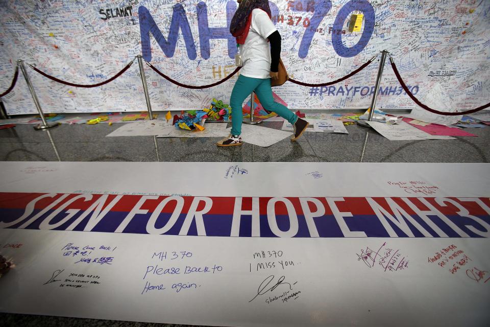 Una mujer camina frente a una cartulina con mensajes de buenos deseos para los pasajeros del avión de Malaysia Airlines que desapareció el 8 de marzo de 2014 cuando iba de Malasia a China, el domingo 16 de marzo, en Sepang, Malasia. (AP Photo/Wong Maye-E)