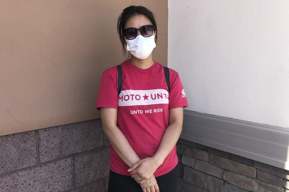 Judy Nguyen, 40, wears a mask and stands by a shopping center wall.