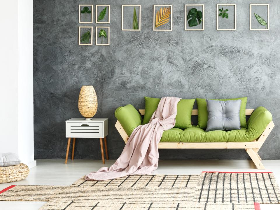 Green couch with pink blanket and end table on left side with picture frames arranged asymmetrically on wall