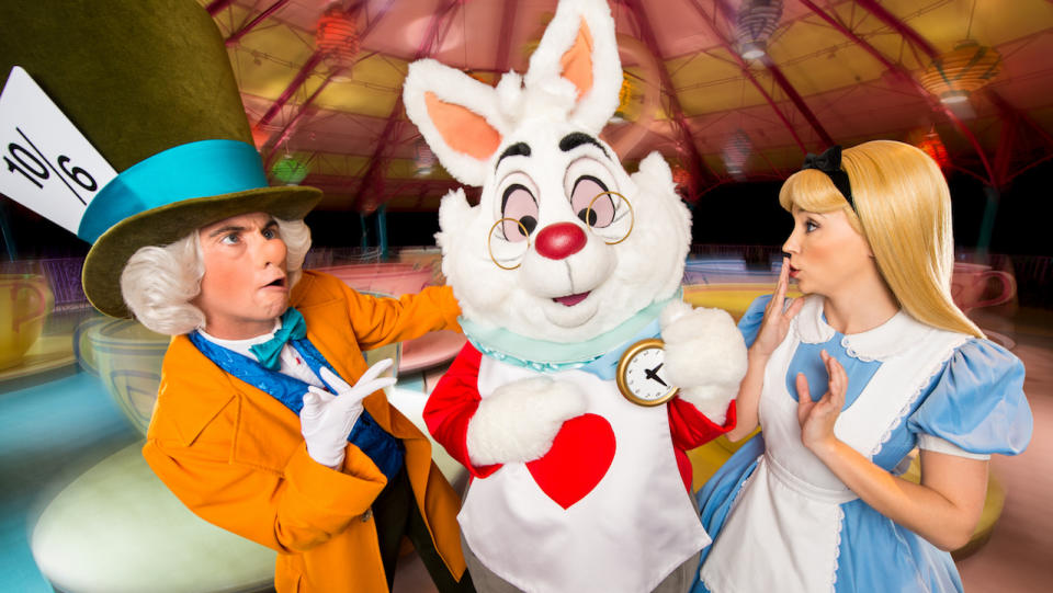 Alice in Wonderland characters posing in front of the Mad Tea Party ride at Disney World.