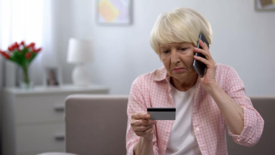 Sad old woman with credit card calling bank support, reporting about money fraud