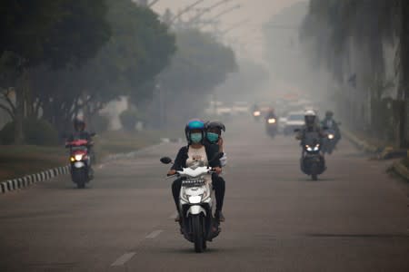 Motorists ride their motorbikes through haze due to a forest fire in Palangka Raya