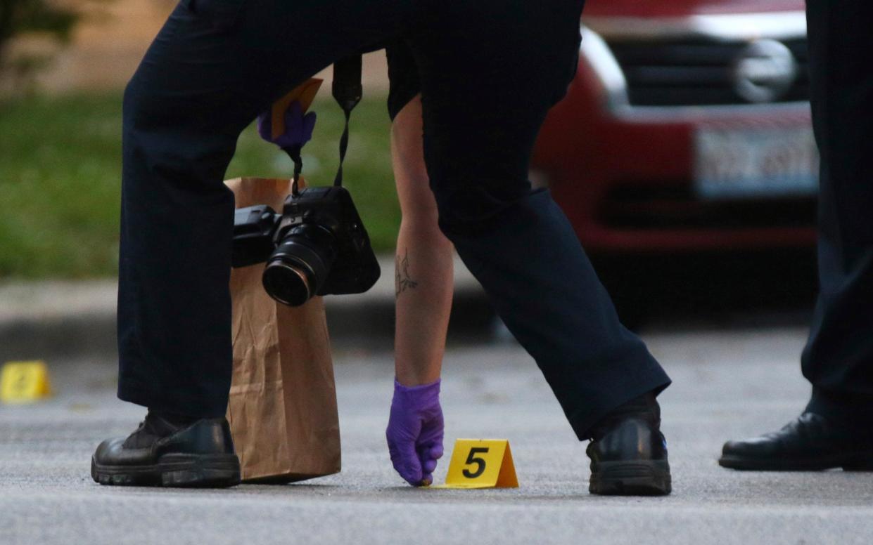 A police forensics investigator picks up a bullet casing at the scene where a three-year-old boy was fatally shot while in the car with his father in Chicago on June 20 - John J. Kim/Chicago Tribune via AP