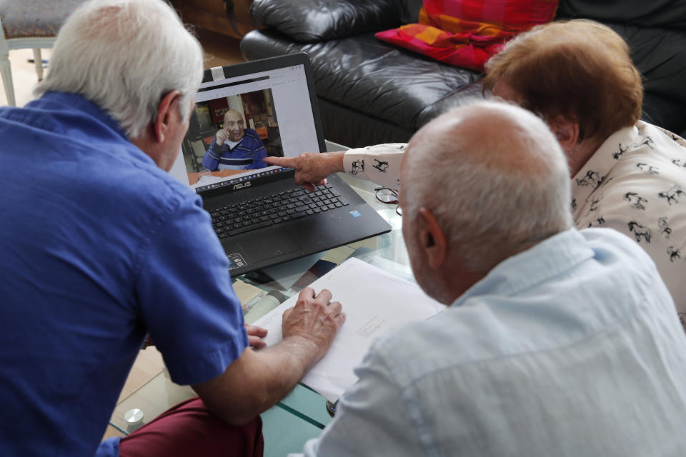 In this photo taken Friday June 5, 2020, Monette Hayoun, Dr Robert Haiun, and Gilbert Haiun, from right, look at photos of their brother Meyer Haiun on a computer during an interview in Ivry sur Seine, south of Paris. Families whose elders died behind the closed doors of homes in lockdown are filing wrongful death lawsuits, triggering police investigations. One suit focuses on the death of Meyer Haiun, a severely disabled 85-year-old in a Paris home managed by a Jewish charitable foundation headed Eric de Rothschild, scion of Europe's most famous banking dynasty. (AP Photo/Francois Mori)