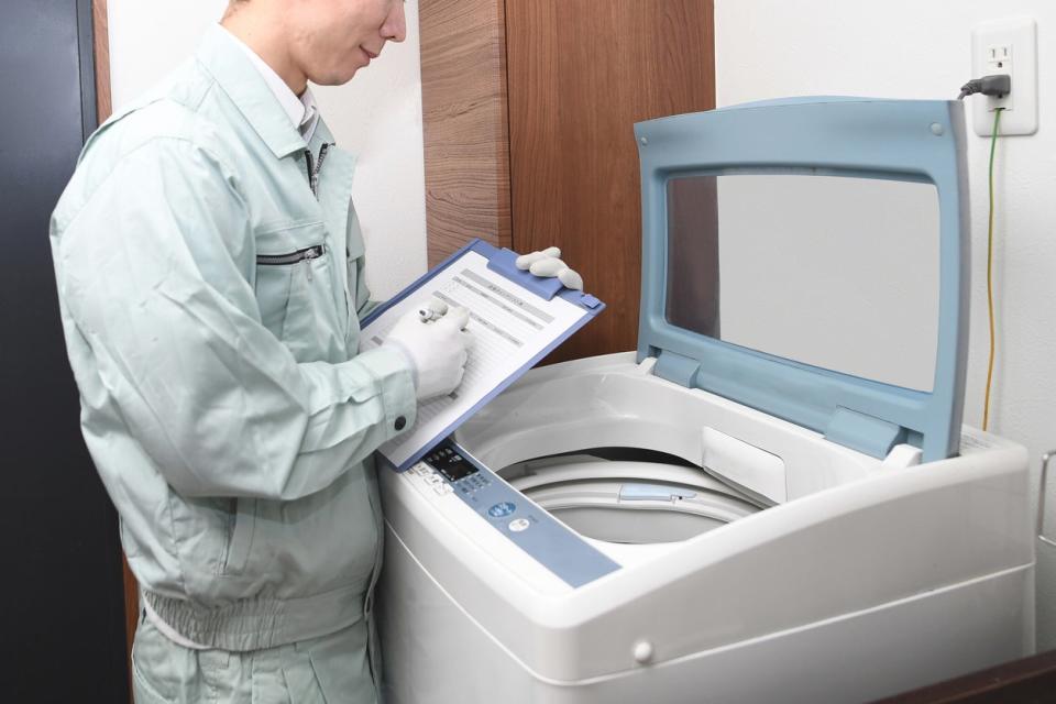 A person in a jumpsuit holds a clipboard while inspecting a dryer.