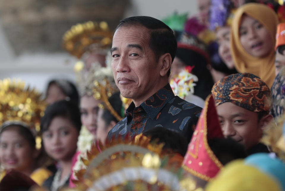 In this Oct. 7, 2019, photo, Indonesian President Joko Widodo reacts as he walks past Indonesian children in traditional dresses during an event at the presidential palace in Bogor, Indonesia. Known for his down-to-earth style with a reputation for clean governance, Widodo's signature policy has been improving Indonesia's inadequate infrastructure and reducing poverty, which afflicts close to a tenth of Indonesia's nearly 270 million people. But raising money would be harder at a time of global economic slowdown, major trade conflicts and falling exports. (AP Photo/Dita Alangkara)