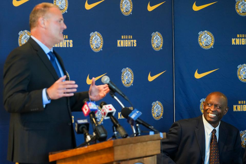 Pat Knight, Marian University’s new men’s basketball head coach, speaks at the podium during a press conference as Steve Downing, Marian University director of athletics, smiles in the background, Friday, May 10, 2024, in the Peyton Manning Children’s Hospital Hall of Champions at Marian University in Indianapolis.