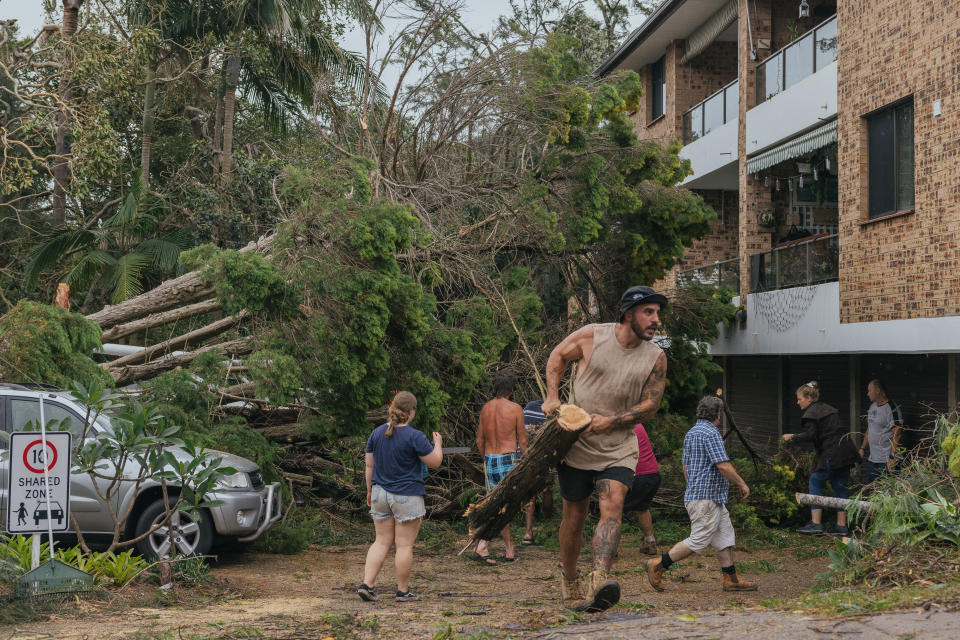 A man carries a fallen branch as community members help clean up debris near Pittwater Road, Narrabeen, on Sunday.