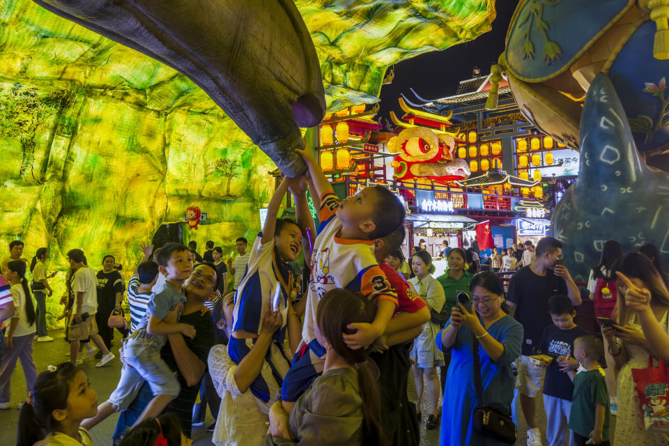 Visitors lift their children to torch a dinosaur figure on display in a new night market during a weeklong national holiday in Nanning in south China's Guangxi Zhuang Autonomous Region on Sept. 30, 2023. Tourism in China bounced back to pre-pandemic levels during a recent eight-day national holiday, giving a temporary boost to the nation's flagging economy. (Chinatopix via AP)