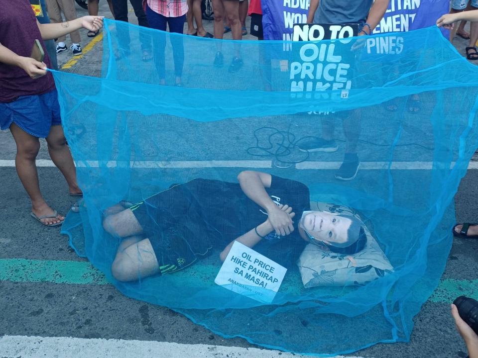 A protester wearing a mask bearing the face of Philippine President Rodrigo Duterte pretends to sleep under a mosquito net to symbolize his inaction on the fuel price increase on October 29, 2021 in Metro Manila, Philippines. Duterte says he wants out of the presidential palace by April, and plans to sleep &#x00201c;wherever God takes him.&#x00201d; (Source: KABATAAN PARTYLIST/Facebook)