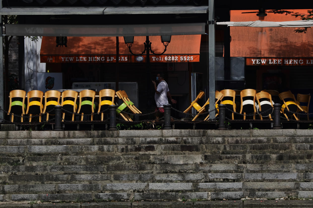 A man wearing protective mask walks past stacked chairs outside a restaurant on May 20, 2021 in Singapore. Singapore enters a month long heightened alert from May 16 to June 13 to curb the spread of COVID-19 cases in the local community. New restrictions on movements and activities have been introduced such as limiting social interaction to two, prohibiting dining out and a reduced operating capacity at shopping malls and attractions. (Photo by Suhaimi Abdullah/NurPhoto via Getty Images)