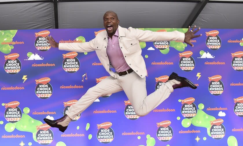 A Black man in a white suit leaps through the air as he arrives at an awards show