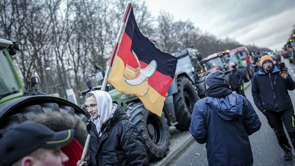 A demonstrator walks in Berlin, on Monday, carrying a German flag with a banana on it. Farmers have gathered in the capital to protest planned subsidy cuts by the federal government, including for agricultural diesel. - Kay Nietfeld/picture-alliance/dpa/AP