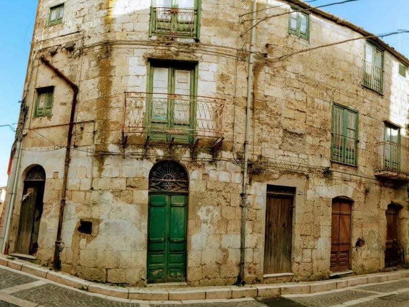 An old building with yellowed white brick and rusted fixtures on a street corner with a green door that Daniels owns.