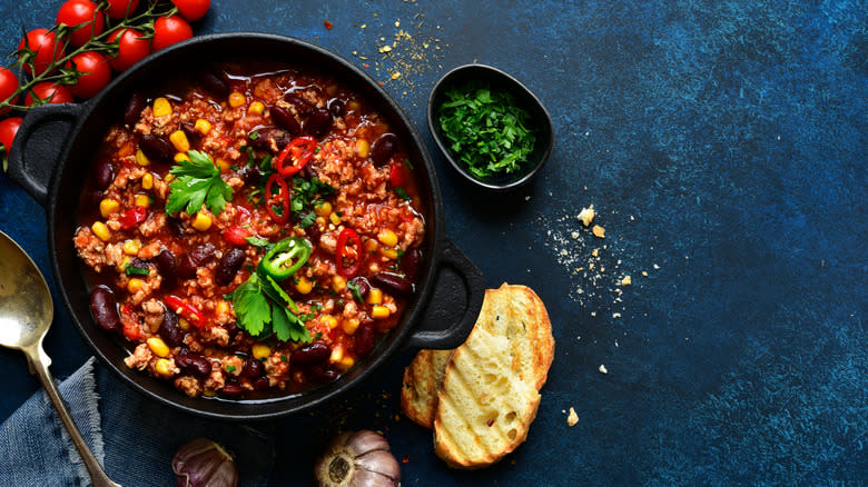 chili in skillet with bread, tomatoes and herbs
