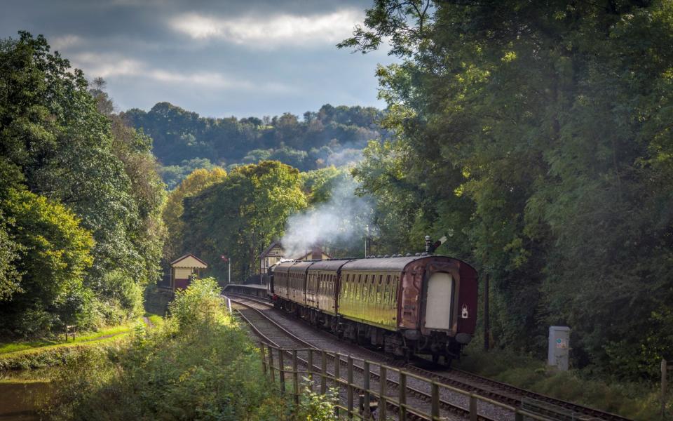 Consall station on the Churnet Valley Railway with a steam train passing by the Caldon canal in Staffordshire. - Alamy Images 