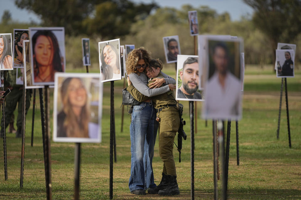 Israelíes se abrazan entre las fotos de fallecidos y rehenes del asalto de Hamás al festival de música Nova, en el sur de Israel, que están expuestas en el lugar donde se celebrará el evento, cerca del kibbutz de Re'im, el 28 de noviembre de 2023. (AP Foto/Ohad Zwigenberg)