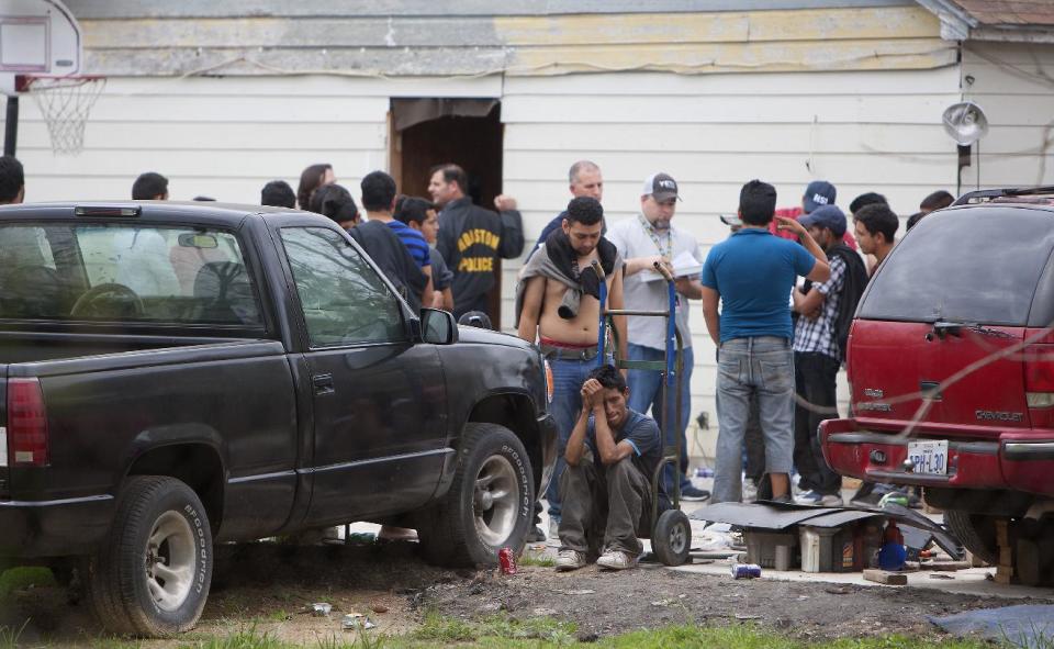 People wait outside a house, Wednesday, March 19, 2014, in southeast Houston. A house overflowing with more than 100 people presumed to be in the United States illegally was uncovered just outside Houston on Wednesday, a police spokesman said. The suspected stash house was found during a search for a 24-year-old woman and her two children that were reported missing by relatives Tuesday after a man failed to meet them, said a spokesman for the Houston Police Department. (AP Photo/Houston Chronicle, Cody Duty)