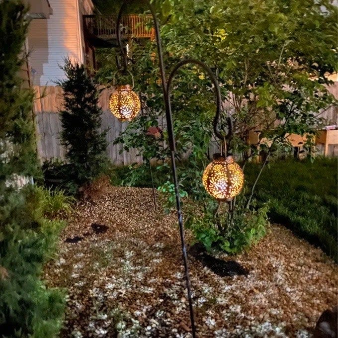 a reviewer photo of two of the lanterns hanging in a yard