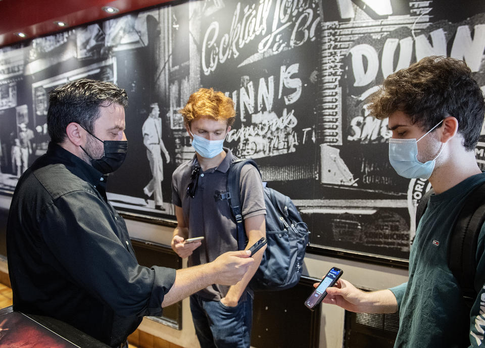 Jimmy Staveris, left, manager of Dunn's Famous restaurant scans the COVID-19 QR code of a client in Montreal on Sept. 1, 2021, as the Quebec government's COVID-19 vaccine passport comes into effect. Residents older than 12 must have the passport to be seated inside or on the patios of restaurants, bars, concert halls, outdoor events with more than 50 people, and most other public places that are not deemed essential. Outsiders do not need and cannot get the passport but must present vaccine proof as well as an ID showing a home address outside Québec. (Graham Hughes/The Canadian Press via AP)